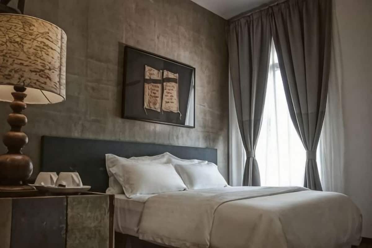 A hotel room with a bed, a lamp, a framed picture, and a window with curtains.
