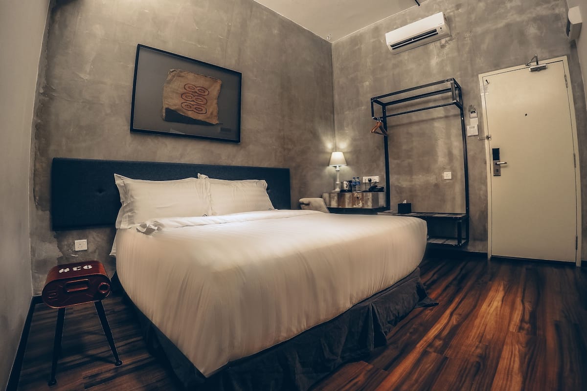A hotel room with a bed, a nightstand, a wall-mounted air conditioner, a door, and a framed picture on the wall.