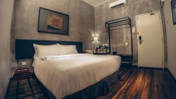 A hotel room with a bed, a nightstand, a wall-mounted air conditioner, a door, and a framed picture on the wall.