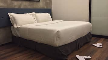 Una cama bien hecha con falda oscura, un cuadro en la pared y un par de zapatillas en el suelo.