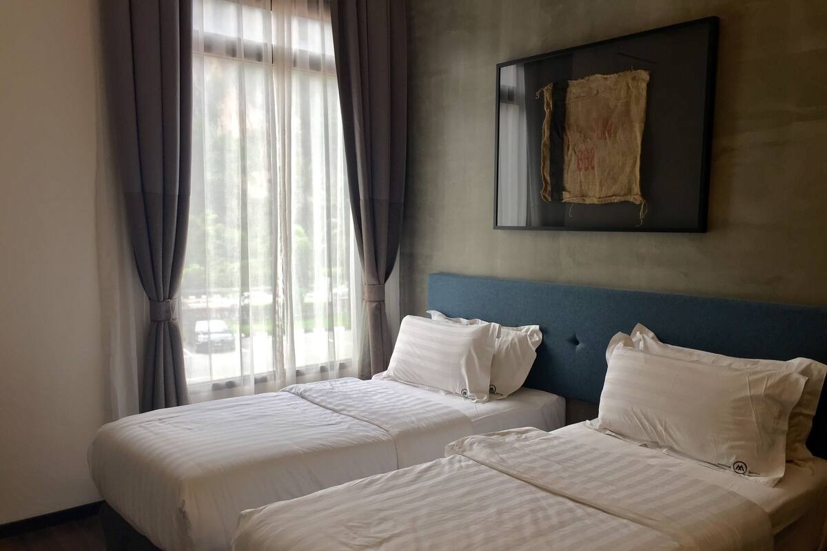 A hotel room with two beds, a large window with curtains, a headboard, and a framed picture on the wall.