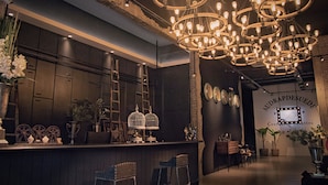 A bar area with a dark wood bar counter, multiple hanging light fixtures, and a wall with a sign reading "AUDRAPDESUDE Costumes & Costumes." - Merton Hotel Ipoh (Ipoh)