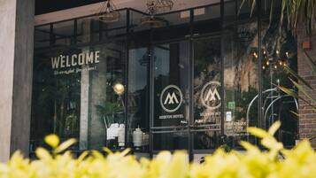 A modern hotel entrance with a 'WELCOME' sign, a logo, and a 'PULL' sign for the door.
