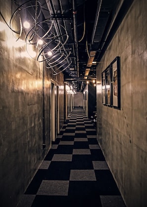 Un couloir doté d’un sol à carreaux, de luminaires métalliques au plafond et de tableaux encadrés accrochés aux murs.