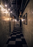 Un couloir doté d’un sol à carreaux, de luminaires métalliques au plafond et de tableaux encadrés accrochés aux murs.