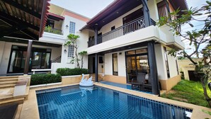 Ein modernes Gebäude mit zwei Stockwerken, einem Schwimmbad, Außenmöbeln und einem Balkon.