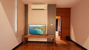 Ein Hotelzimmer mit Holzboden, einem flachbildfernseher an einer Holzablage, einer Klimaanlage an der Wand und einer Tür zu einem anderen Raum.
