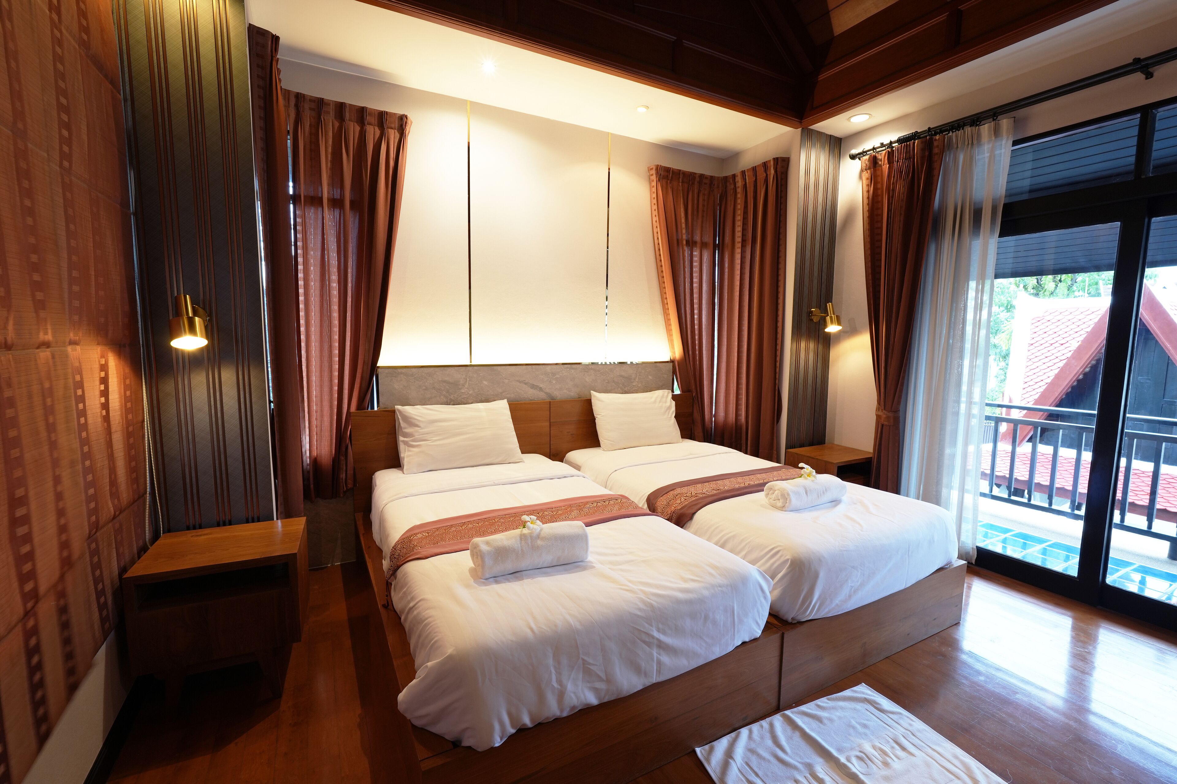 A double bed with two pillows, a wooden nightstand, a wooden bench, and a large window with curtains.