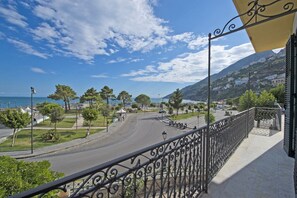 Ein Balkon mit Metallgeländer, der auf eine Küstenstraße mit Bäumen und einem klaren Himmel blickt.