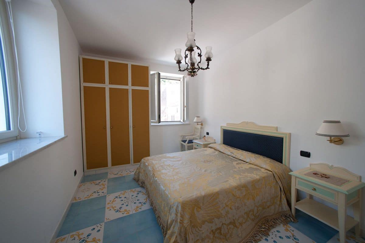 Un dormitorio con cama, mesita de noche, cómoda, ventana y candelabro.