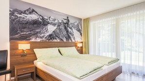 Ein modernes Hotelzimmer mit einem großen Bett, einem hölzernen Kopfteil und einem Wandgemälde mit Bergmotiven.