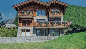 Ein zweistöckiges Holzhaus mit Balkonen, Stein Fundament und einem Bergpanorama.