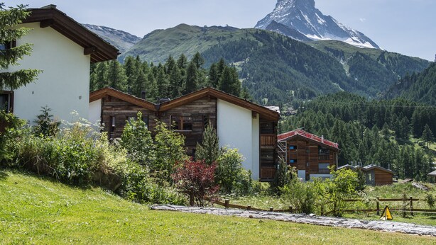 Eine Berghütte mit Holzhütten und Blick auf einen markanten Berggipfel.