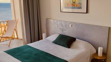 Une chambre d’hôtel avec un lit, une chaise, un tableau et une vue sur la mer.