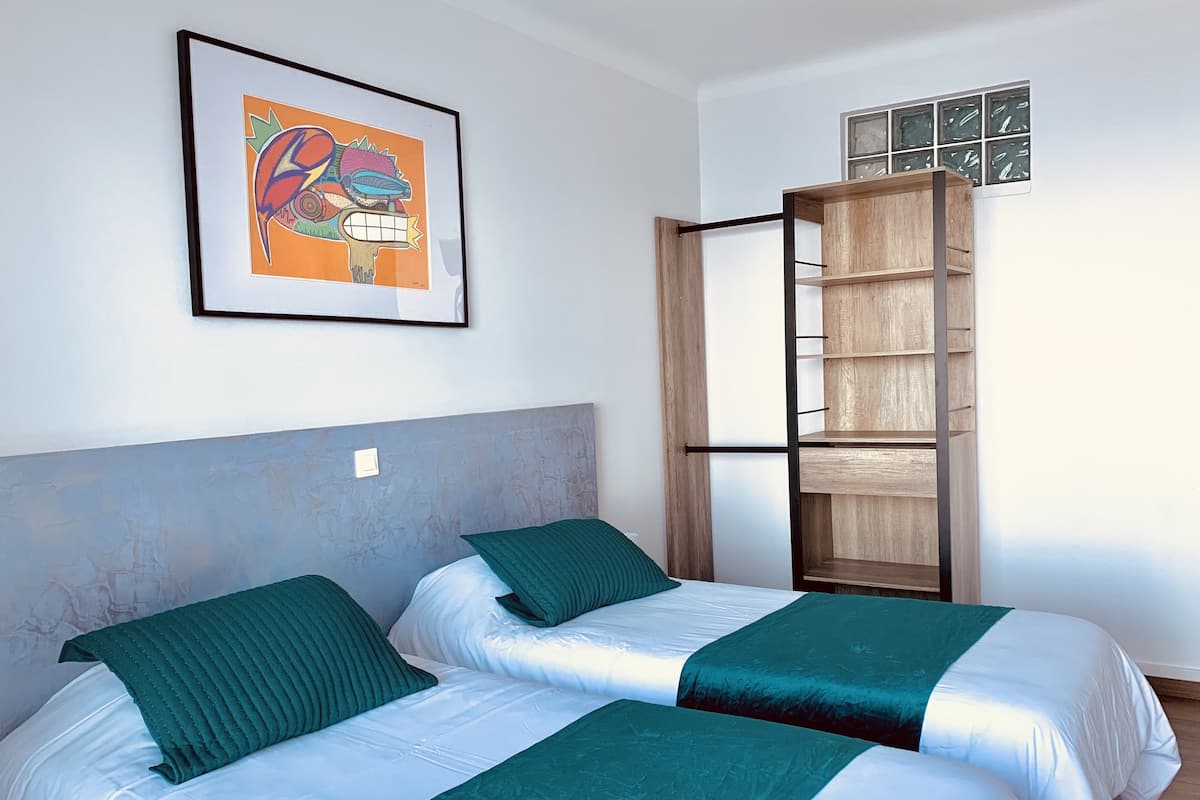 A room with two beds, a wooden shelf unit, and a framed artwork on the wall.