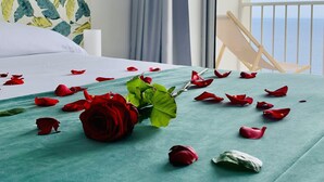 Una cama bien hecha con una colcha verde, una rosa roja solitaria y pétalos de rosa esparcidos.