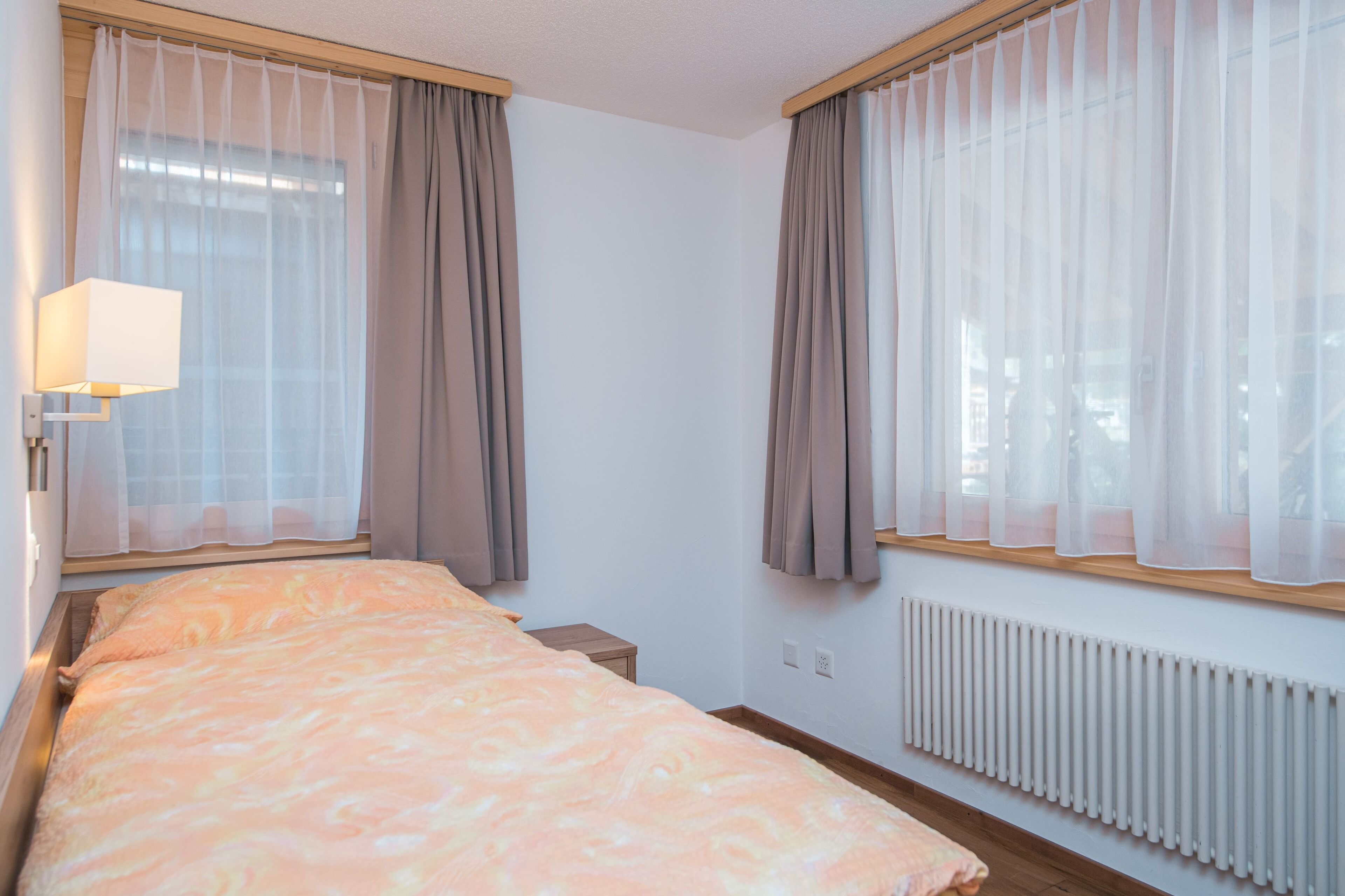 A hotel room with a bed, a nightstand, a lamp, and a radiator.