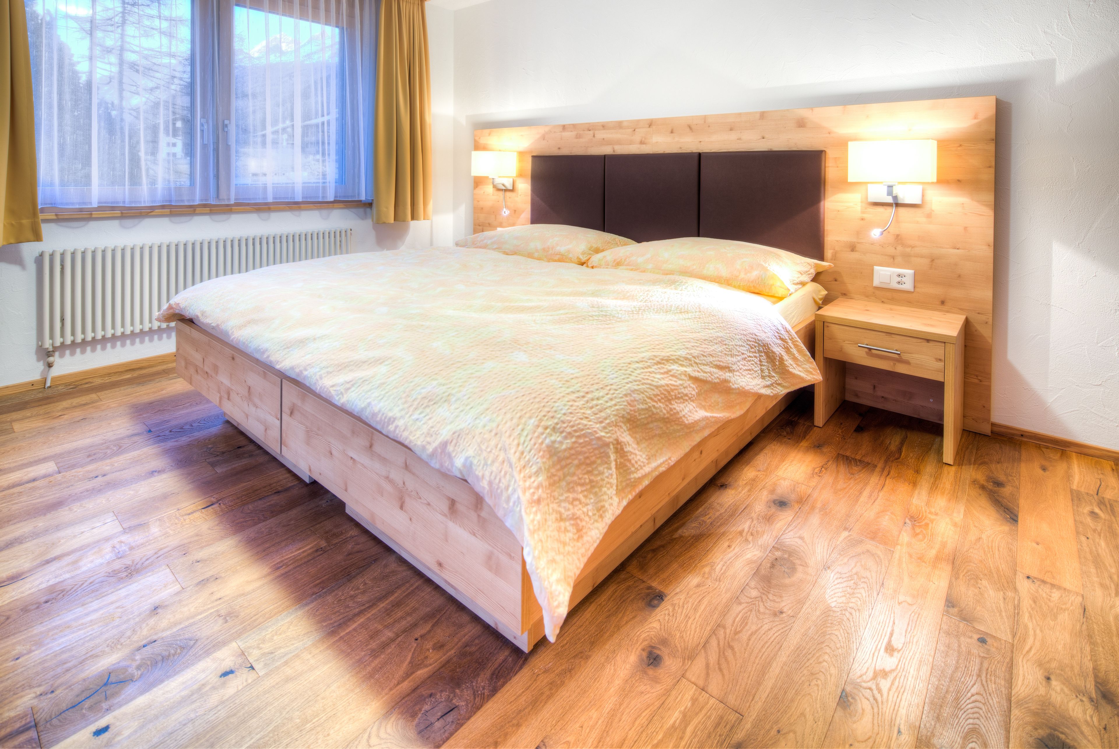 A wooden-framed bed with a headboard, two bedside tables, and a window with curtains.