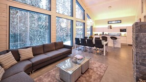 A modern interior with a large window, a sofa, a dining area, and a kitchen. - Villa Borealis (Pälkäne)
