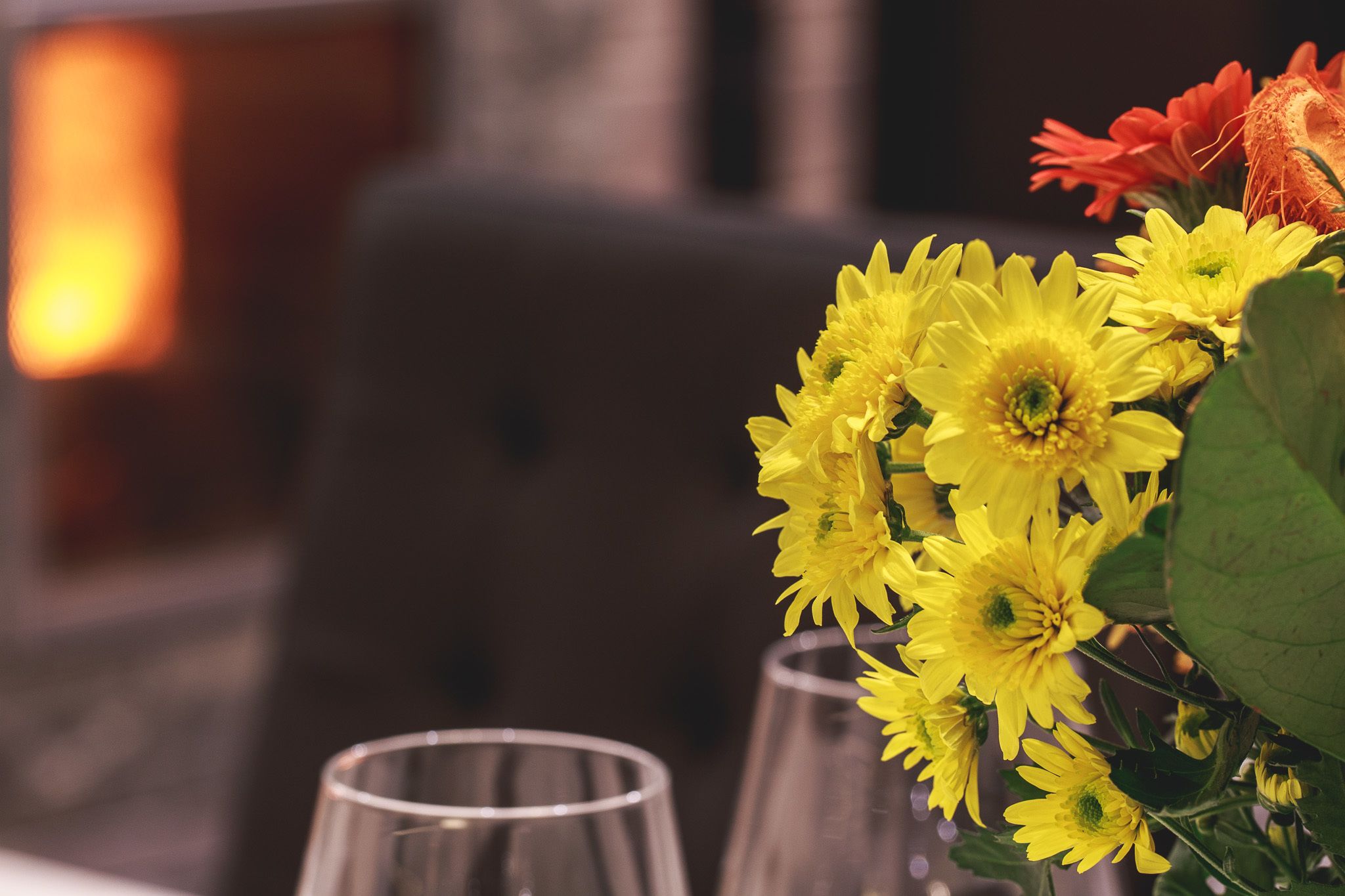 Een tafel met een vaas gele bloemen en twee lege glazen.