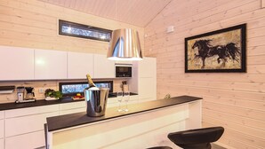 A modern kitchen with a central island, stainless steel appliances, and a wooden wall with a framed painting. - Villa Borealis (Pälkäne)