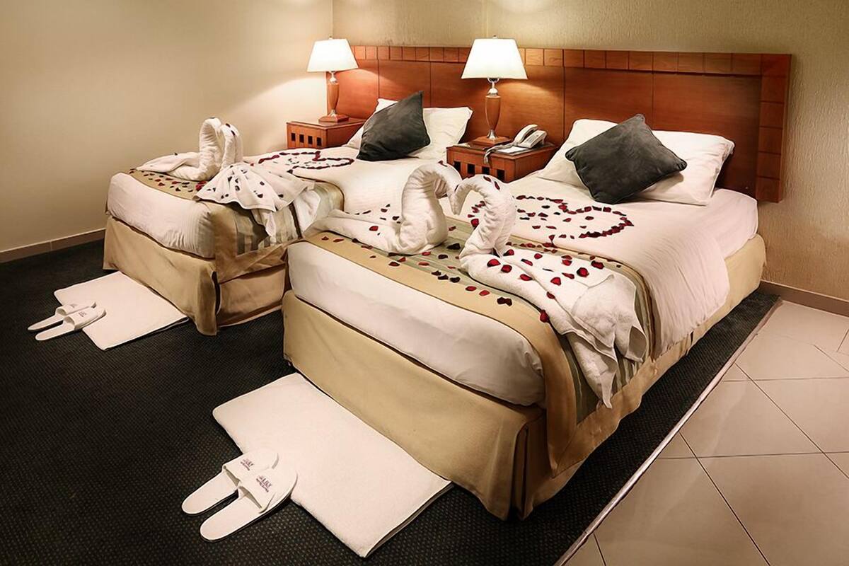 A hotel room with two beds, each with a wooden headboard, bedside tables with lamps, and a telephone.