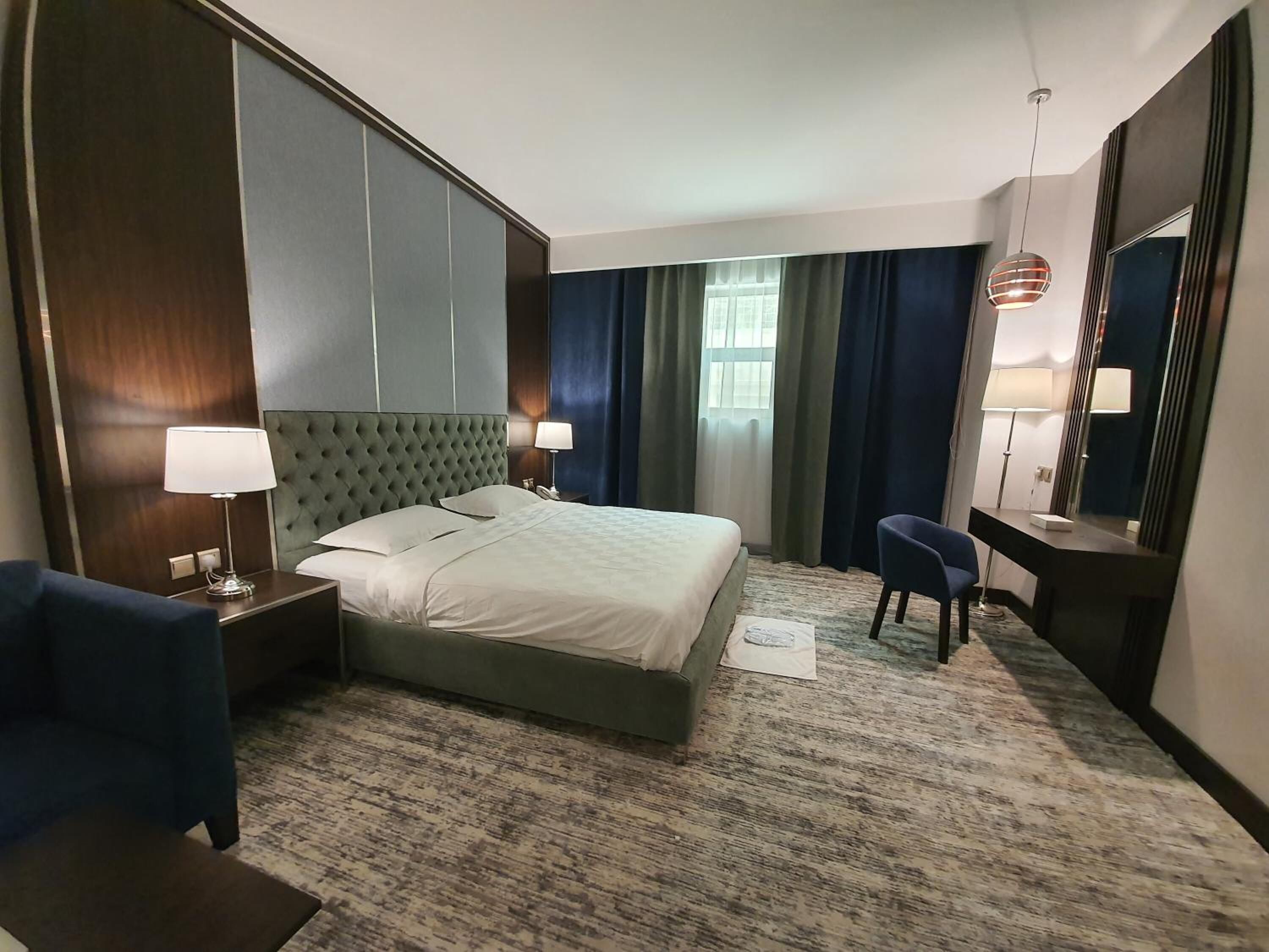 A hotel room with a large bed, a desk, a chair, a lamp, and a mirror.