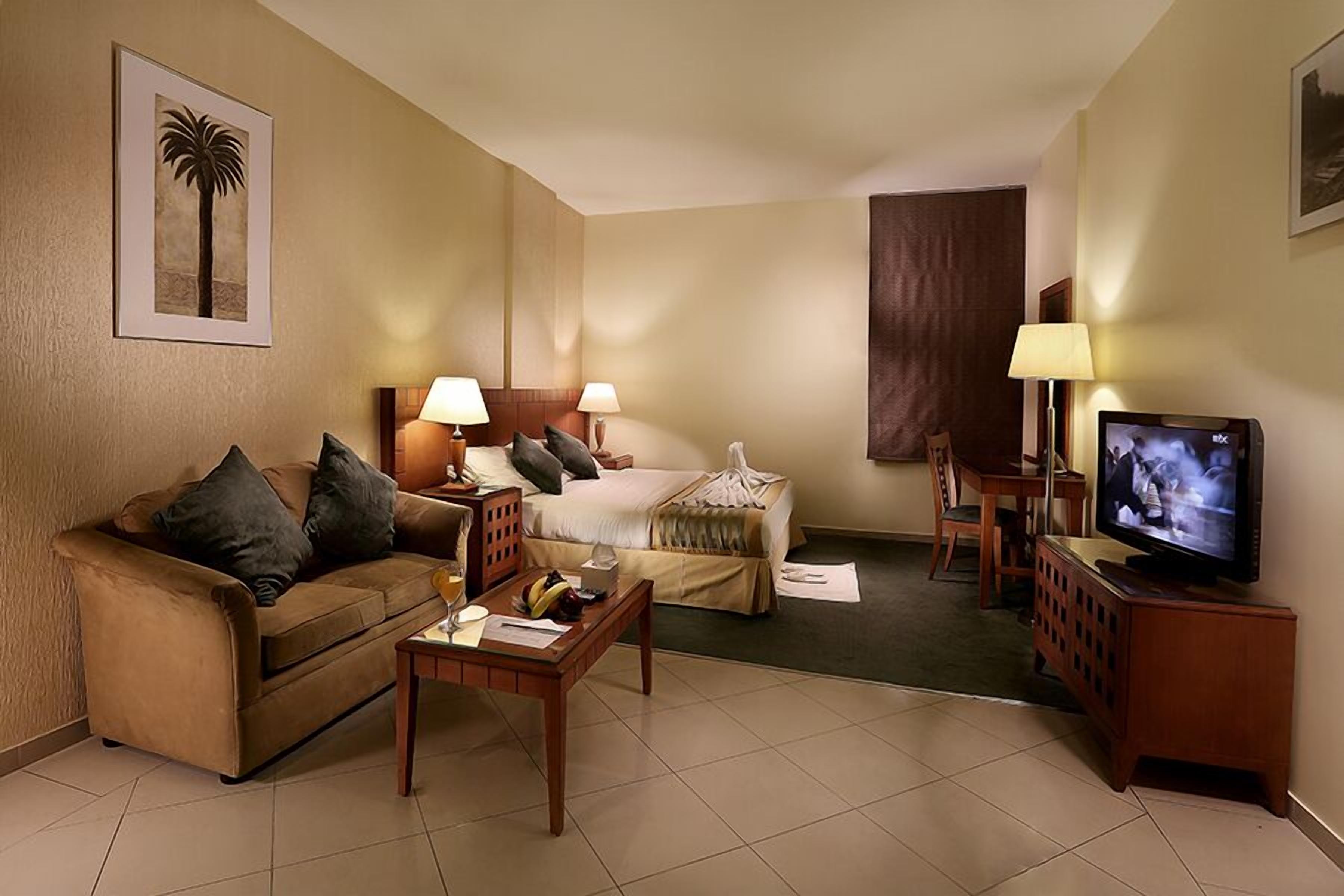 A hotel room with a sofa, a bed, a TV, and a desk.