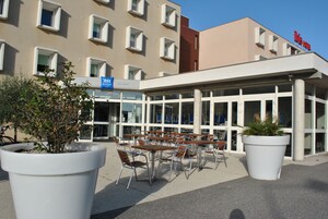 Un área de estar al aire libre con mesas y sillas frente a un edificio con múltiples ventanas y un letrero que dice "ibis budget".