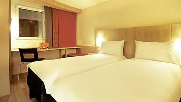 Ein Hotelzimmer mit Doppelbett, Schreibtisch mit Stuhl, Fenster mit Jalousien und Nachttisch mit Lampe.
