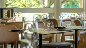 Een restaurant met gedekte tafels, helder servies en uitzicht op groen door grote ramen.