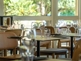 Un restaurante con mesas dispuestas para comer, cristalería transparente y vistas a la vegetación a través de grandes ventanales.
