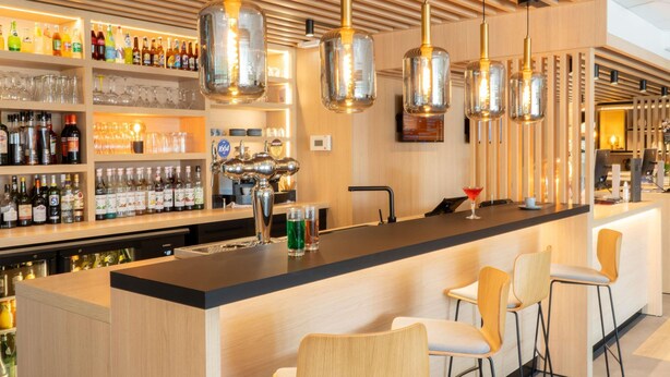 Een bar met een houten toonbank, barstoelen en hangende hanglampen.