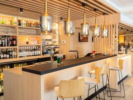 Una zona de bar con mostrador de madera, taburetes y lámparas colgantes.