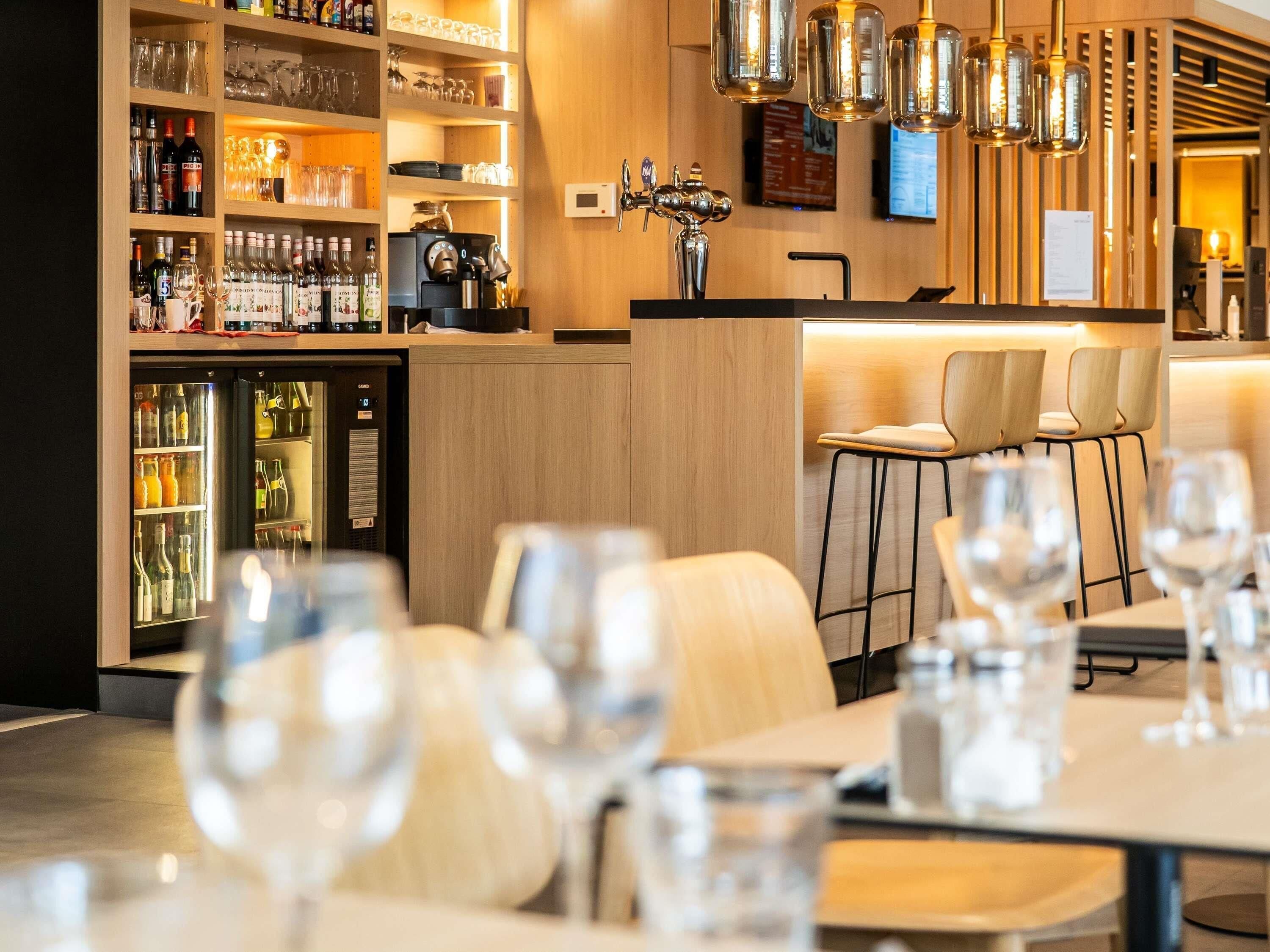 A bar area with shelves of bottles and glasses, a coffee machine, and a seating area with tables and chairs.
