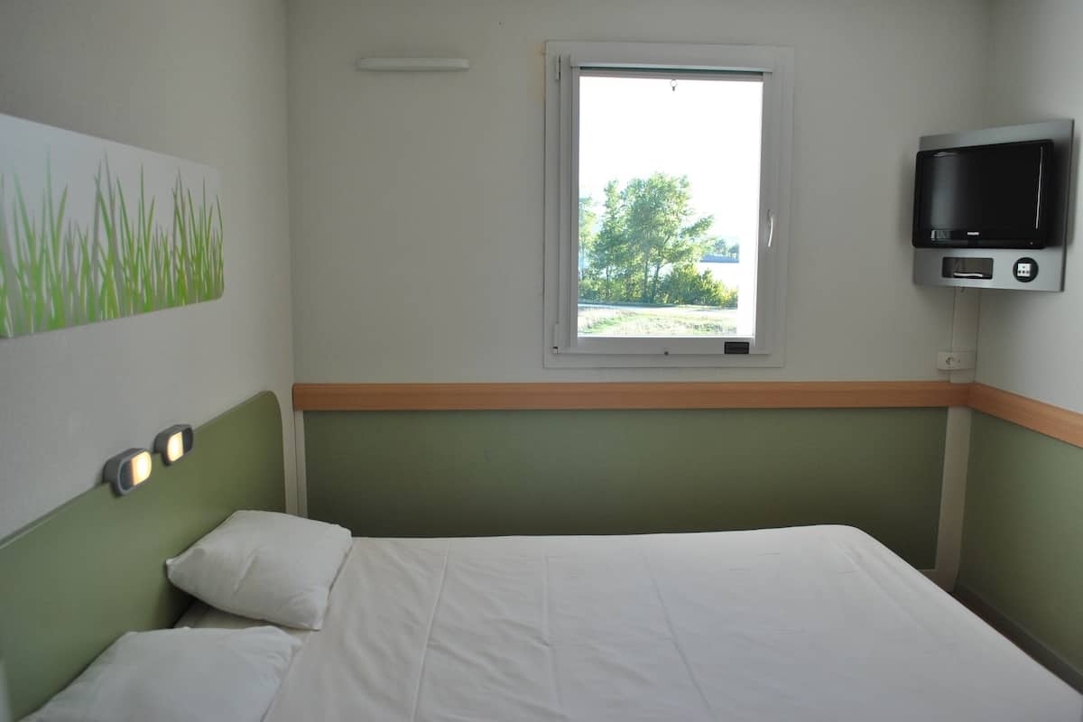 Una habitació d'hotel amb un llit, una finestra i un televisor fixat a la paret.