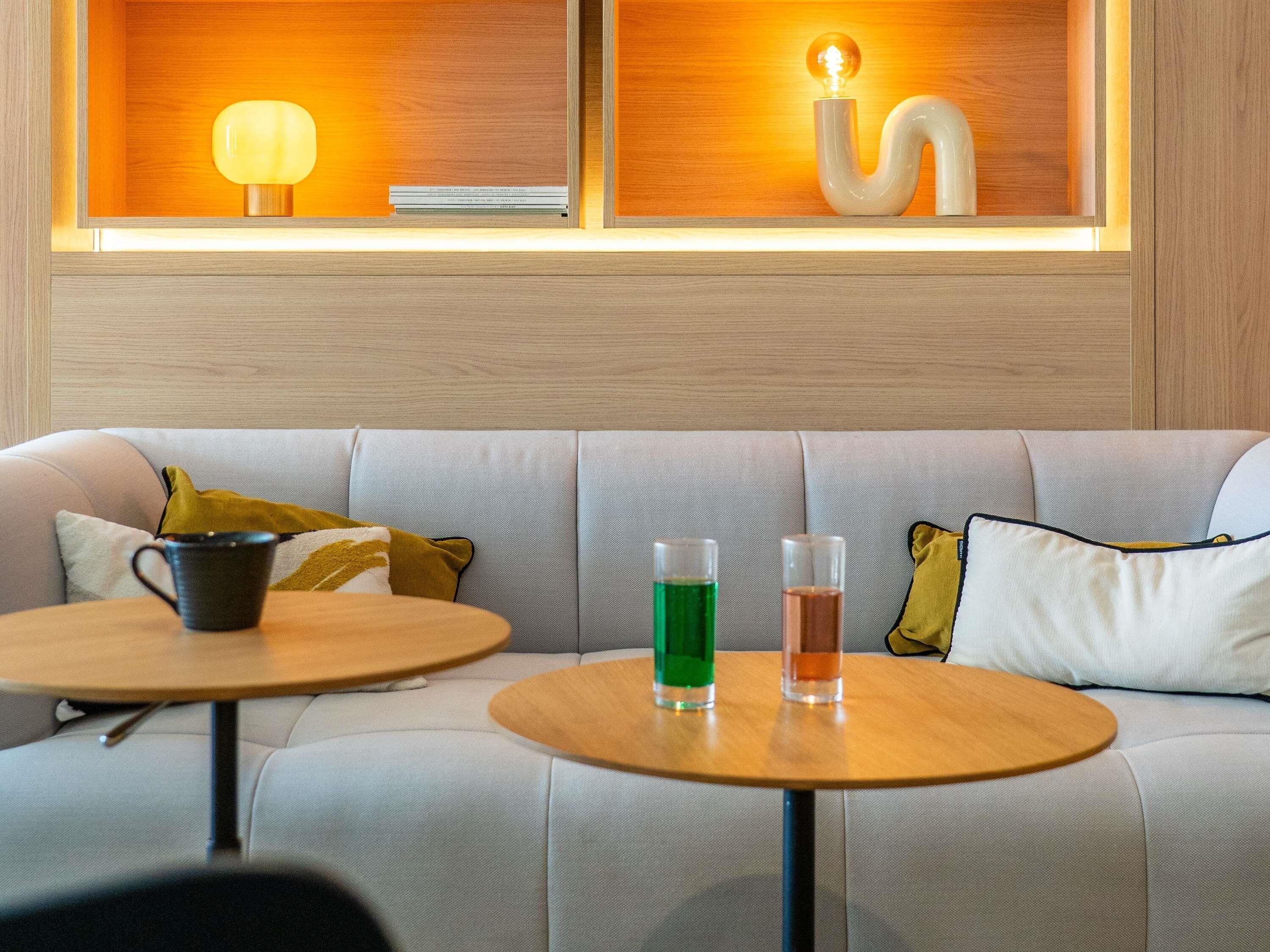 A modern interior with a sofa, two round tables, and a wall-mounted shelf with decorative items.