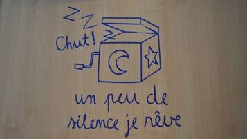 Une surface en bois ornée d’un dessin représentant un cube, un croissant de lune et une étoile, ainsi que du texte suivant : « Chut ! Un peu de silence, je rêve. »