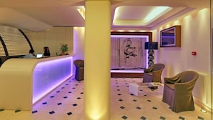 Un hall d’hôtel moderne avec un comptoir d’accueil, un espace salon et une grande œuvre d’art accrochée au mur.