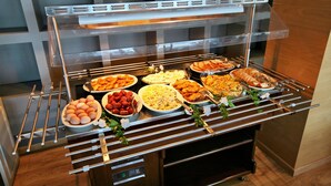 Un buffet proposant divers plats, notamment des œufs, des pâtes et de la viande.