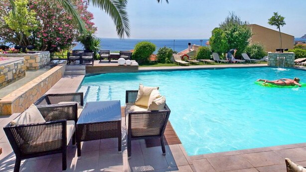 Un espace piscine avec des chaises longues et une table, une vue sur l’océan et un mur en pierre.