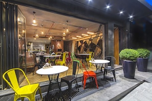 An outdoor cafe with multiple tables and chairs, a staircase, and potted plants.
