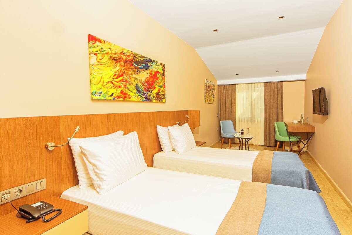 Quarto de hotel com duas camas, uma mesa, uma cadeira, um telefone e um quadro na parede.