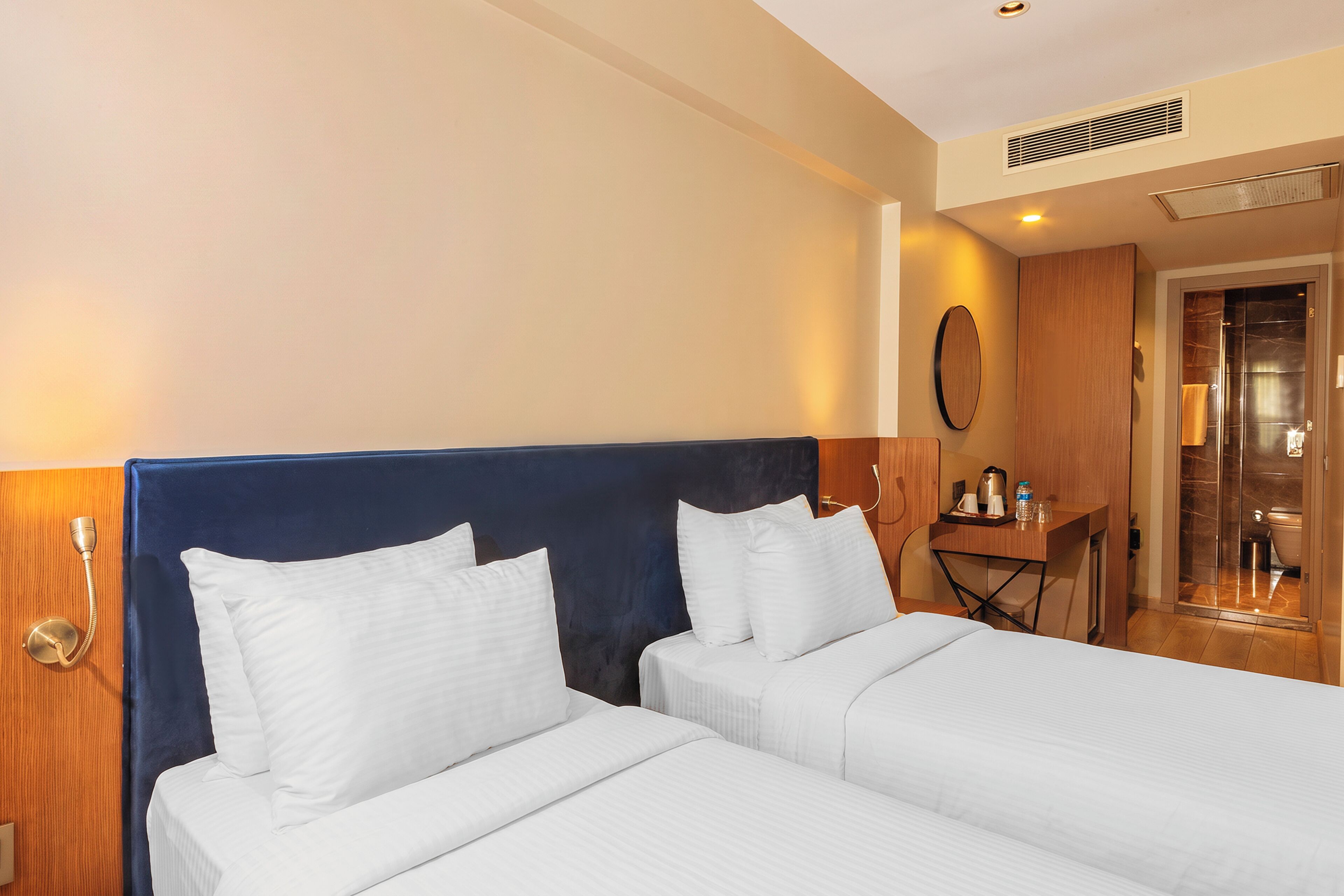 A hotel room with two beds, a wooden headboard, a small table with a kettle, cups, and a bottle.