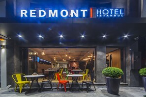 L’extérieur de l’hôtel Redmont à Istanbul présente un design moderne, avec une enseigne bien visible, un espace extérieur aménagé avec des chaises colorées et de grands pots de plantes.