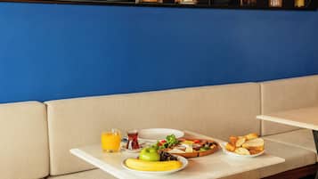 Un coin repas avec une table mise pour le petit-déjeuner, un verre de jus d’orange et une assiette de fruits.