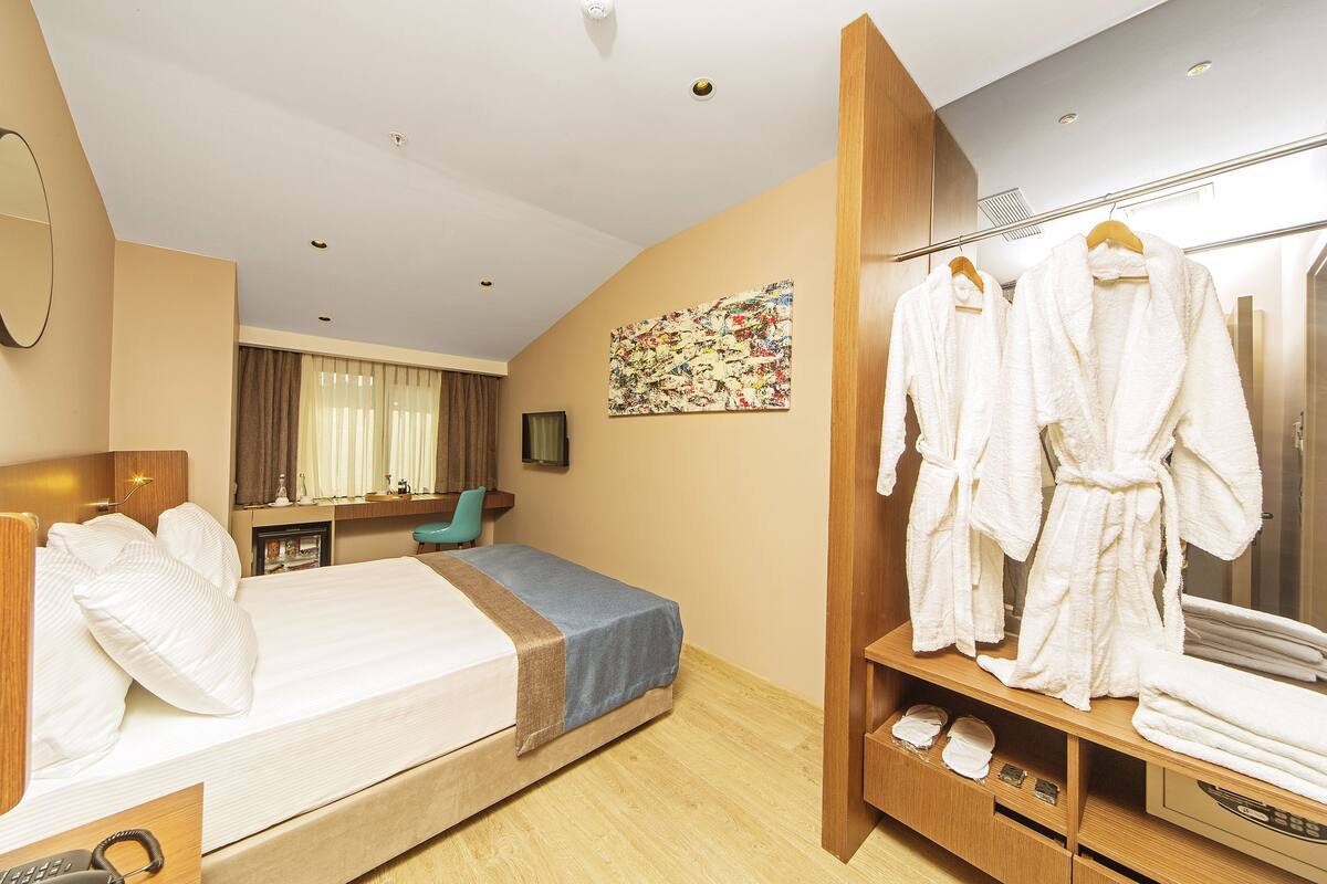 Quarto de hotel com cama, guarda-roupa de madeira, espelho e um quadro na parede.