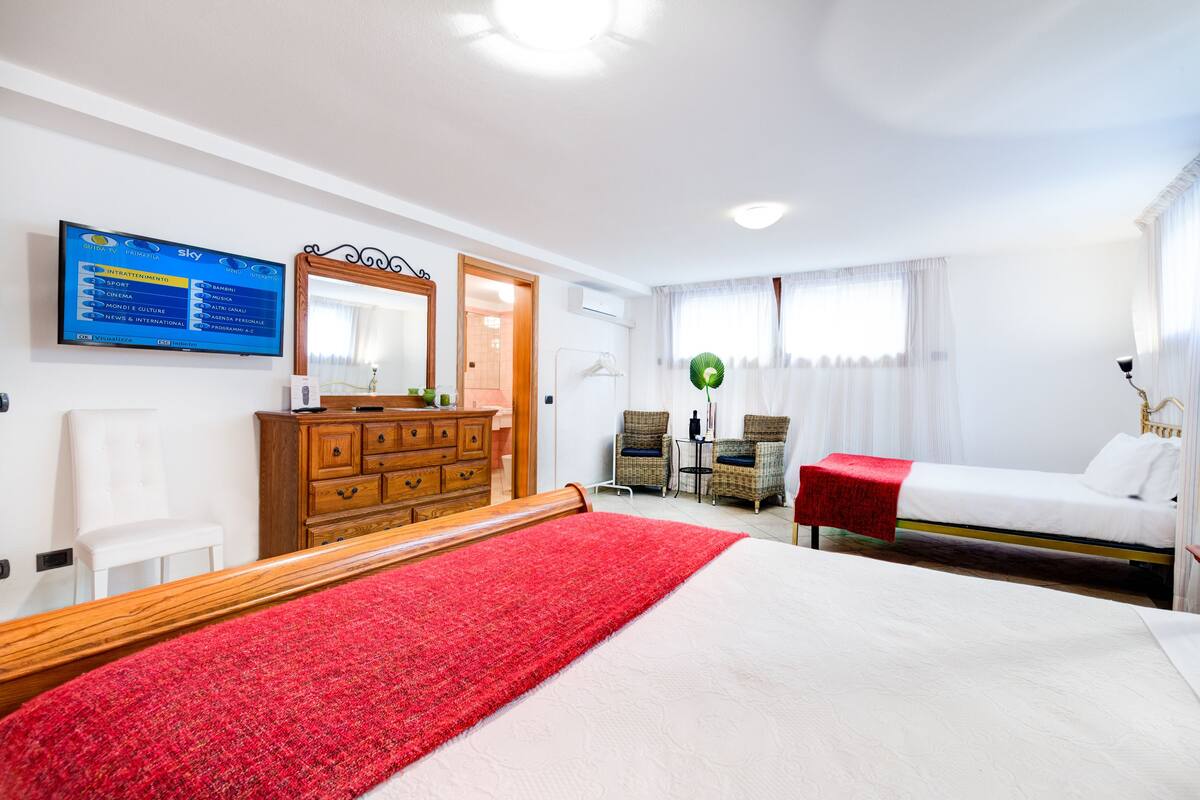 Una habitación de hotel con cama, cómoda, televisor y ventana con cortinas.
