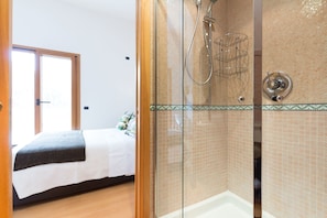 Una habitación con cama, zona de ducha con puerta de cristal y pared con azulejos.