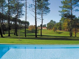 Una piscina con césped y árboles al fondo.